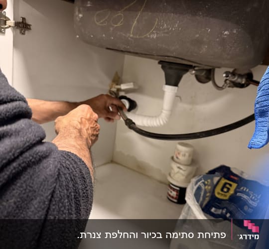 אדם מתקן צינור מתחת לכיור במטבח